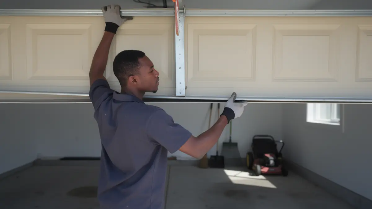 A technician in gloves adjusts a beige garage door.